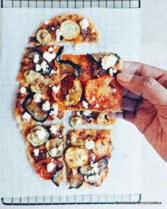 Flatbread with roasted vegetables and feta, sliced with hand holding up a slice